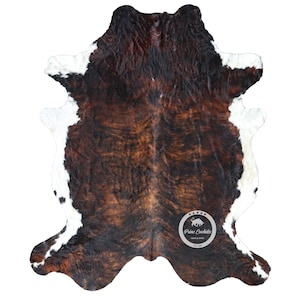 以下が含まれることがあります： 茶色と白の牛革の敷物で、自然な斑点模様があります。敷物は約1.5メートル×2.1メートルです。