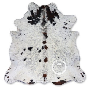 以下が含まれることがあります： 白地に黒と茶色の斑点のある牛革の敷物。この敷物は自然で素朴な外観で、どんな部屋にもウエスタンスタイルのアクセントを加えるのに最適です。