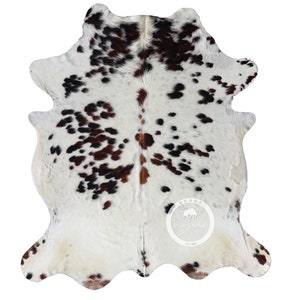 以下が含まれることがあります： 白地に茶色と黒の斑点のある牛革の敷物。敷物は約1.5メートル×1.8メートルです。