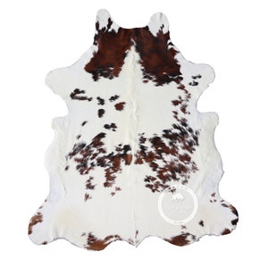 以下が含まれることがあります： 白地に茶色と黒の斑点のある牛革の敷物。この敷物は、柔らかく高級感のある天然の皮革で作られています。