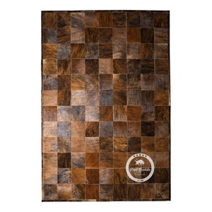 May include: A brown and black patchwork cowhide rug with a square pattern. The rug has a distressed look and is made of natural materials.