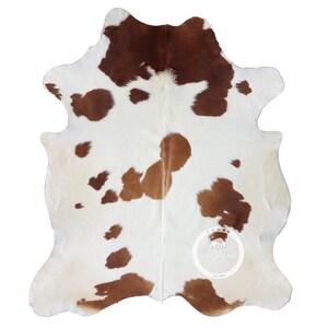 以下が含まれることがあります： 白地と茶色の斑点とパッチのある牛革ラグ。ラグは、丸みを帯びたエッジと自然な質感を持つ不規則な形状をしています。茶色の部分は上部と端に集中し、小さな斑点が表面全体に散らばっています。約150cm x 180cm。