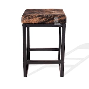Puede incluir: Un taburete cuadrado con asiento de piel de vaca marr&oacute;n y negra y estructura de metal negro. El asiento presenta el texto blanco NEW YORK STOOLS impreso en el lado derecho. El taburete tiene cuatro patas rectas unidas por barras.