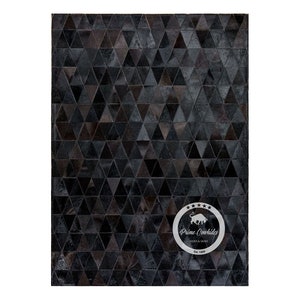 Puede incluir: Alfombra de piel de vaca negra y marrón con un patrón geométrico de triángulos. La alfombra tiene un logotipo en la esquina inferior derecha que dice "Prime Cowhides, Hides & Skins, Est. 1989."