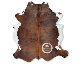 May include: Brown and white cowhide rug with a natural, spotted pattern. The rug is approximately 5 feet by 7 feet.