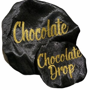 May include: Two black satin hair bonnets with gold glitter lettering. The larger bonnet says "Chocolate" and the smaller bonnet says "Chocolate Drop".