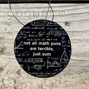 May include: Black and white round ornament with a math pun that reads "not all math puns are terrible, just sum". The ornament is covered in mathematical equations and symbols.