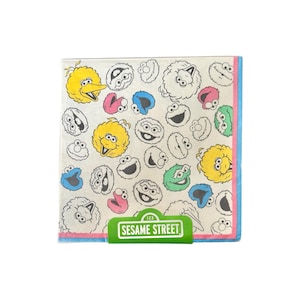 May include: Square paper napkins featuring Sesame Street characters like Big Bird, Cookie Monster, and Elmo. The napkins have a white background with a colorful pattern of the characters and the words "Sesame Street" in a green rectangle.