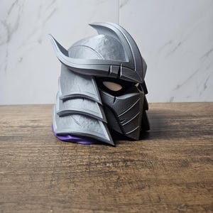 May include: A white ceramic mug with a black handle and the text "But First, Coffee" in a bold, black font. The mug is set against a blurred background, suggesting a cozy setting.