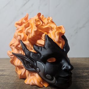 May include: A 3D-printed mask featuring a black face with silver accents and orange, flame-like hair. The mask has pointed ears and a detailed design, likely for cosplay or display.