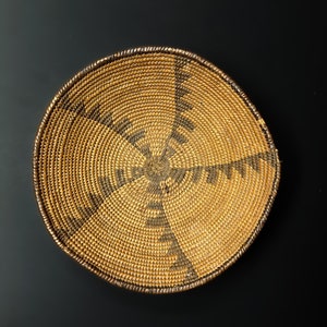 May include: A round woven basket with a brown and tan pattern. The basket is made of natural materials and has a circular shape.