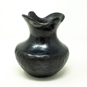 May include: A black ceramic vase with a wide, flared opening and a textured, slightly bumpy surface.