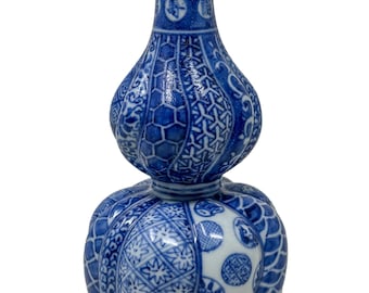 Può includere: Un vaso in porcellana blu e bianco a forma di doppia zucca, caratterizzato da un corpo segmentato decorato con intricati motivi geometrici, disegni floreali e medaglioni circolari contenenti caratteri cinesi sul collo stretto.