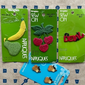 May include: Three sew-on appliqués on green cards: a yellow banana and green pear, red cherries with green leaves, and the word "Devil" in red and black. Also, four decorative details with brown and tan accents.