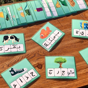 Pode incluir: Um conjunto de cartões de memória coloridos com letras árabes e imagens de vários objetos, como um peixe, uma vaca, um sapato, uma árvore, um presente e um guarda-chuva. Os cartões são projetados para ensinar alfabetização árabe a crianças pequenas.