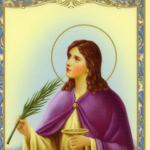 May include: A woman in a purple robe holds a golden chalice and a palm branch. She has long brown hair and is looking to the right. The background is a light yellow with a halo above her head.