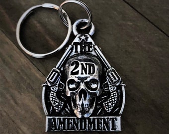 Może przedstawiać: Srebrny metalowy brelok do kluczy z motywem czaszki i napisem "The 2nd Amendment".