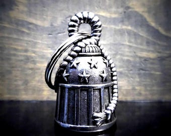 May include: A silver-toned metal bell keychain featuring a patriotic design with embossed stars on the upper section and vertical stripes on the lower section. A thick, textured rope-like detail wraps around the top and side of the bell.