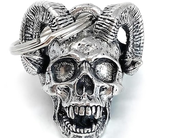 May include: A silver skull keychain with horns. The skull has a detailed design with a toothy grin.