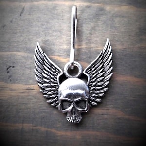 May include: Silver skull with wings zipper pull charm. The skull has a detailed design and the wings are spread out.
