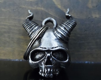 May include: Silver skull motorcycle handlebar bell with horns. The bell has a detailed skull design with horns and a ring for attaching to a motorcycle handlebar.