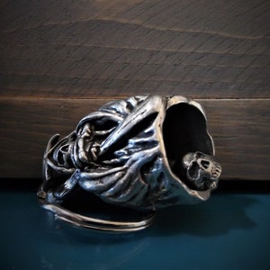 Puede incluir: Llavero de calavera de plata con un dise&ntilde;o detallado de una figura encapuchada. La calavera es visible dentro de la capucha.