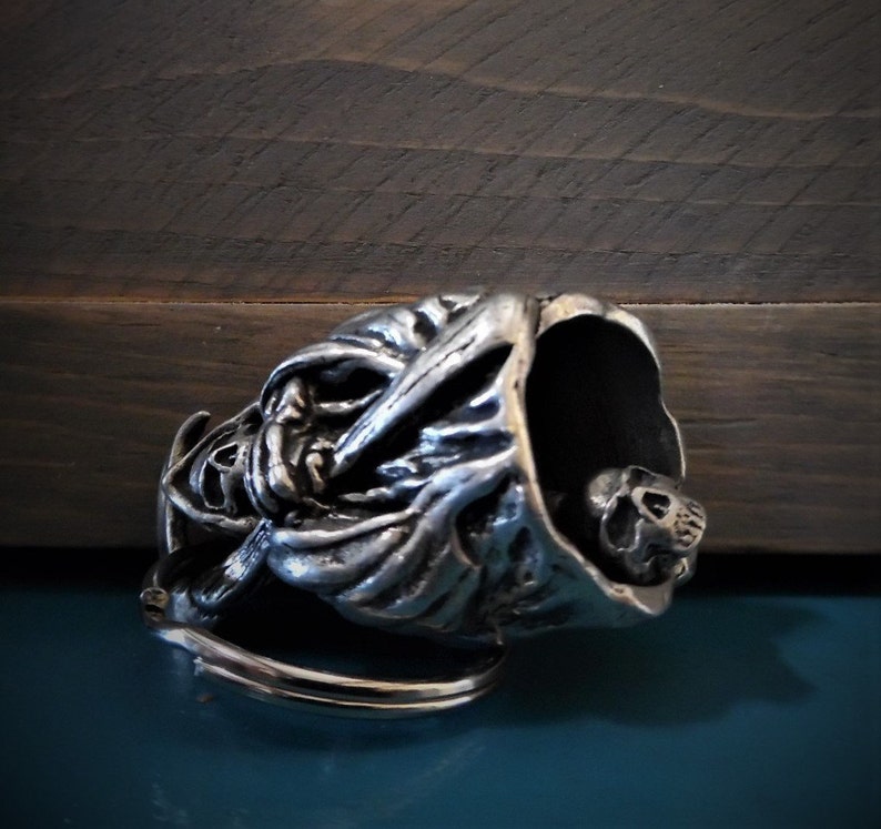 Puede incluir: Llavero de calavera de plata con un dise&ntilde;o detallado de una figura encapuchada. La calavera es visible dentro de la capucha.