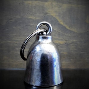 May include: A silver motorcycle bell with a round, domed shape and a ring attached to the top.