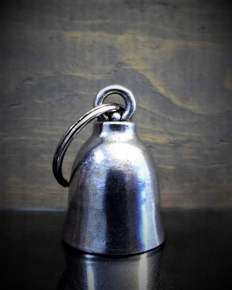 May include: A silver motorcycle bell with a round, domed shape and a ring attached to the top.