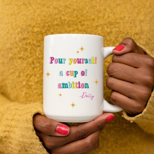 May include: White ceramic mug with a colorful quote that reads "Pour yourself a cup of ambition - Dolly". The quote is in a retro font with stars around it.