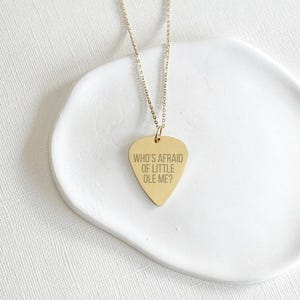 May include: Gold necklace with a guitar pick pendant that says "Who's Afraid of Little Ole Me?"