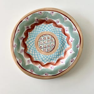 Pu&ograve; includere: Un set di tre tazze in ceramica con una glassa screziata color crema. Ogni tazza presenta un design dipinto a mano diverso: una foglia blu e verde, un fiore giallo e una bacca rossa. Le tazze hanno un design semplice e moderno.