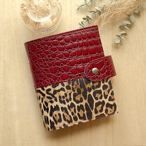 May include: A rectangular notebook featuring a two-tone cover design. The top section has a deep red crocodile-embossed texture, while the bottom section displays a tan and black leopard print pattern. A matching red snap closure secures the cover.