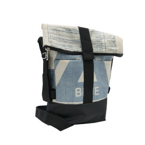 May include: A shoulder bag with a roll-top closure, made from recycled materials. The bag has a blue and white geometric pattern, a black base, and a black adjustable shoulder strap. The word "BLUE" is visible on the front.