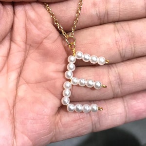 May include: A gold chain necklace with a pearl letter E pendant.