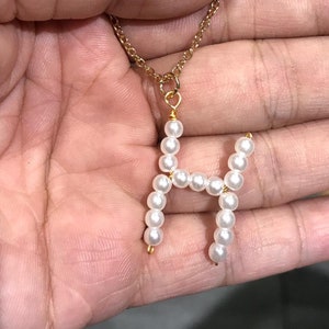 May include: A gold chain necklace with a pendant in the shape of the letter H made of white pearls.
