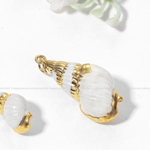 May include: Two gold-coloured seashell charms with white enamel. The larger seashell charm is about 5 cm long and the smaller seashell charm is about 2.5 cm long.