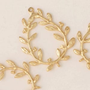 Puede incluir: Siete aros de metal de color dorado en forma de hoja, cada uno con un pequeño bucle en la parte superior para colgar. Los aros están dispuestos en forma de estrella sobre un fondo blanco.