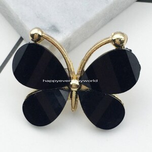 Puede incluir: Adorno de mariposa negro con detalles dorados. La mariposa mide 2,2 x 2,8 mm.