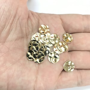 May include: A pile of gold-colored metal round sequins with a hole in the center. The sequins have a hammered texture.
