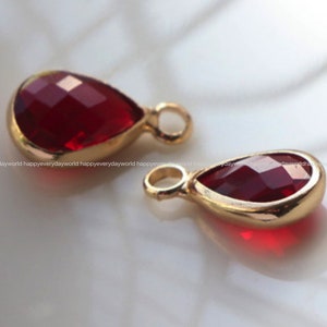May include: Two gold-tone teardrop-shaped charms with red crystal accents. The charms have a loop at the top for attaching to jewelry.