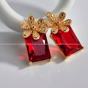 May include: A pair of gold-tone earrings with red rectangular stones and gold flower accents.