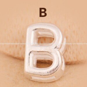May include: Silver charm in the shape of the letter B. The charm is hollow and has a three-dimensional design.