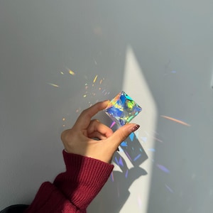 May include: A multifaceted, clear glass geometric prism that refracts light into a vibrant spectrum of colours. The object is shaped like a diamond or octahedron, casting colourful light reflections and shadows onto the surrounding area.
