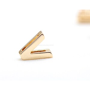 Op de afbeelding: Goudkleurige metalen letter V bedel. De letter is in een eenvoudig, modern lettertype.