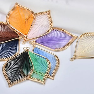 以下が含まれることがあります： 金色の金属フレームにカラフルな糸で包まれた葉の形をしたチャームの詰め合わせ。チャームはオレンジ、ブラウン、ブルー、パープル、グリーン、ホワイトなど、さまざまな色があります。