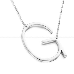 Può includere: Una collana con catena d'argento con un grande ciondolo a forma di lettera G aperta.