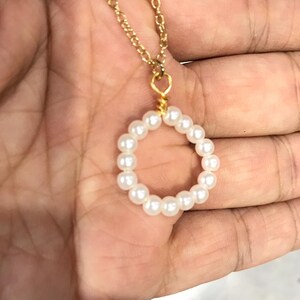 May include: A gold chain necklace with a white pearl circle pendant.