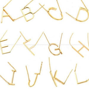May include: Gold-toned alphabet letter necklaces. Each necklace features a simple, modern design of a single letter in a bold, open-style font. The necklaces are perfect for layering or wearing alone.