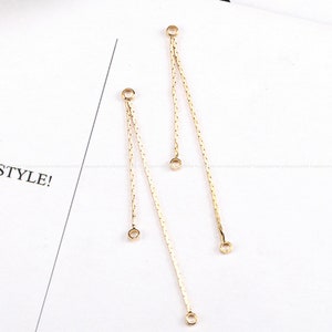 May include: Two gold chain earring components with jump rings at the top and bottom. The chains are delicate and have a slight shimmer.